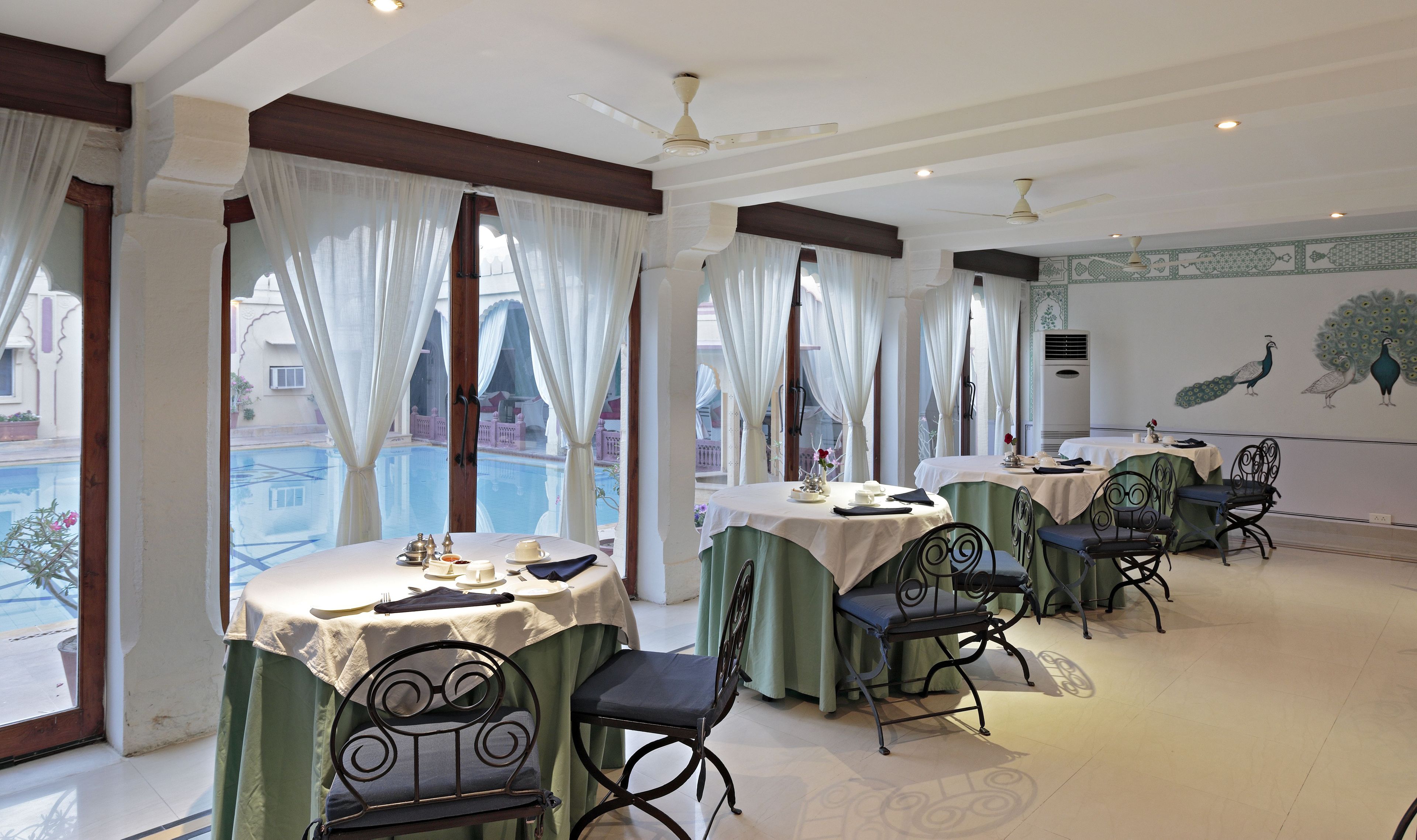 A dining area with tables set for two, featuring green chairs and white tablecloths.