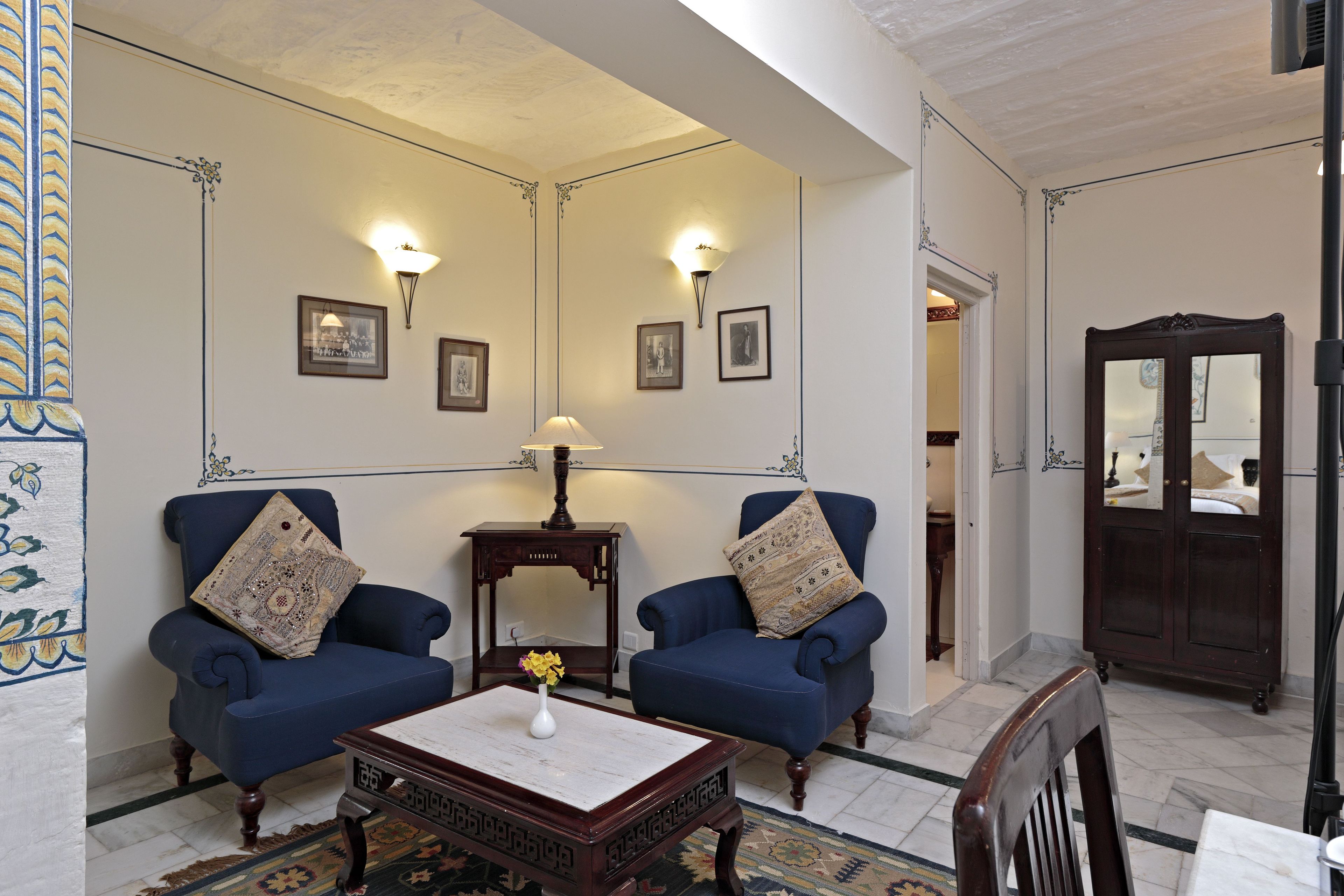 Una habitación con dos sillones azules, una mesa de centro de madera con un florero y un mueble con espejo.