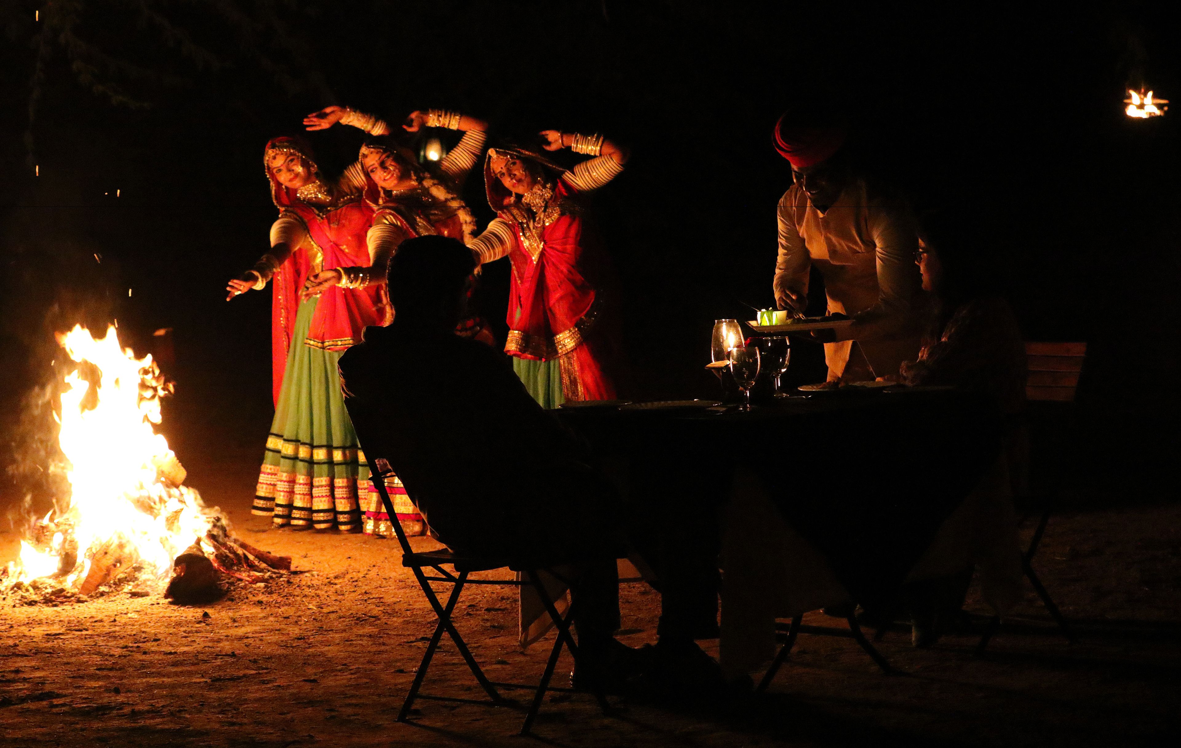 Eine Gruppe von Menschen führt bei Nacht einen traditionellen Tanz um ein Lagerfeuer auf.