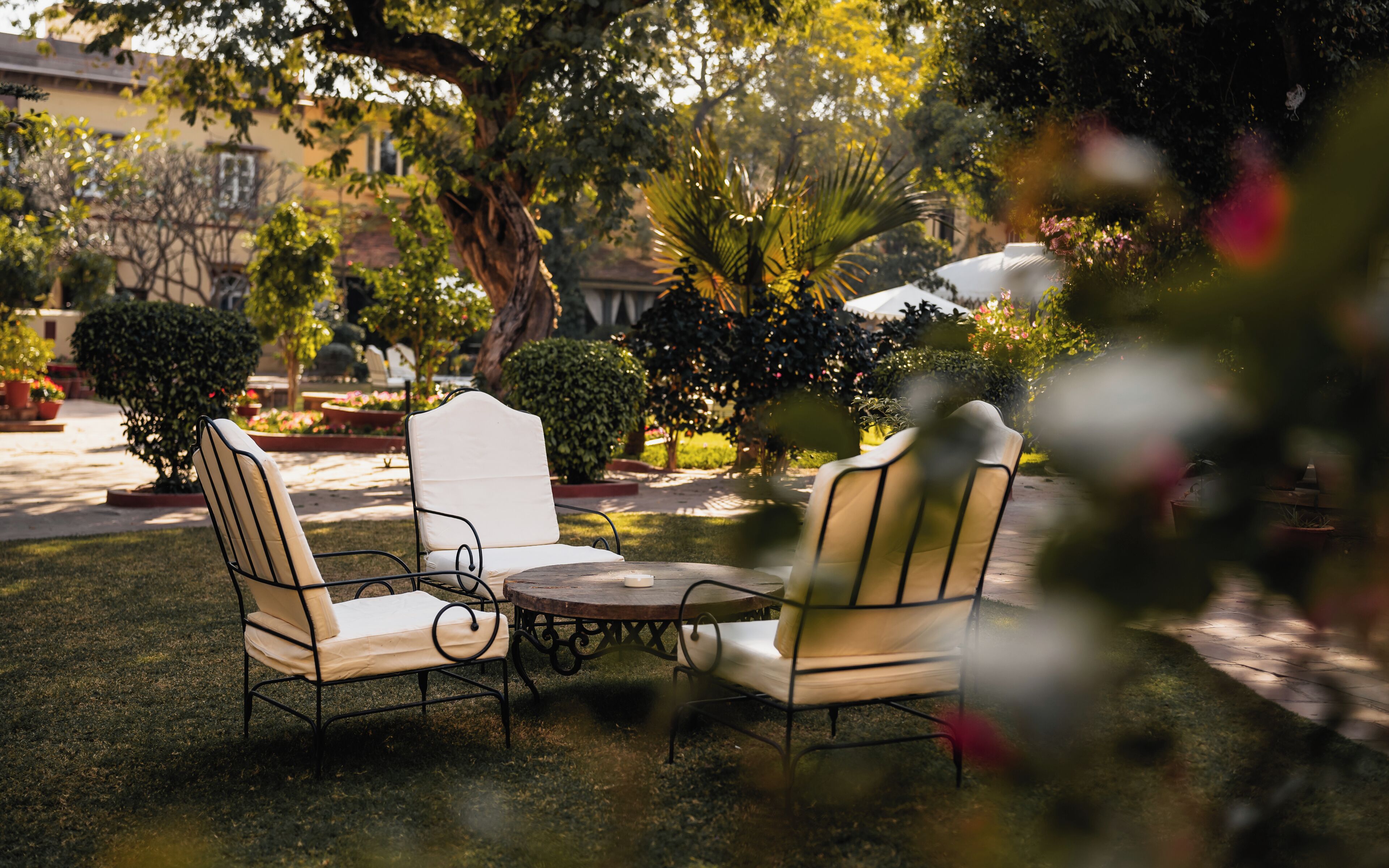 An outdoor seating area with a round table and four chairs, surrounded by well-maintained greenery and trees.