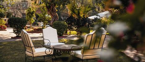 An outdoor seating area with a round table and four chairs, surrounded by well-maintained greenery and trees.