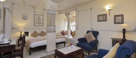 A traditional room with a bed, two blue armchairs, a coffee table, and a patterned rug.