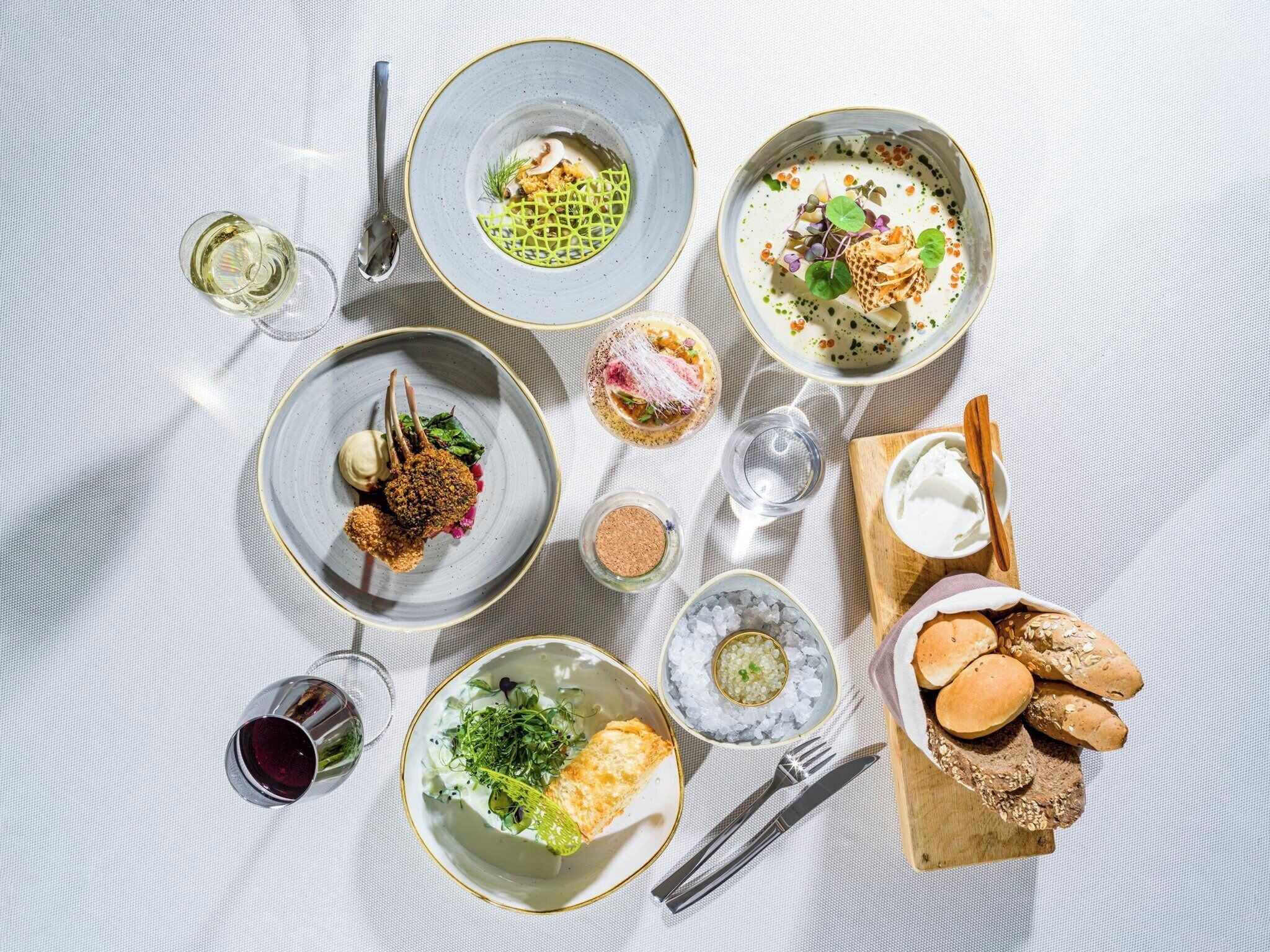 A table with various dishes, a glass of wine, and bread on a textured tablecloth.