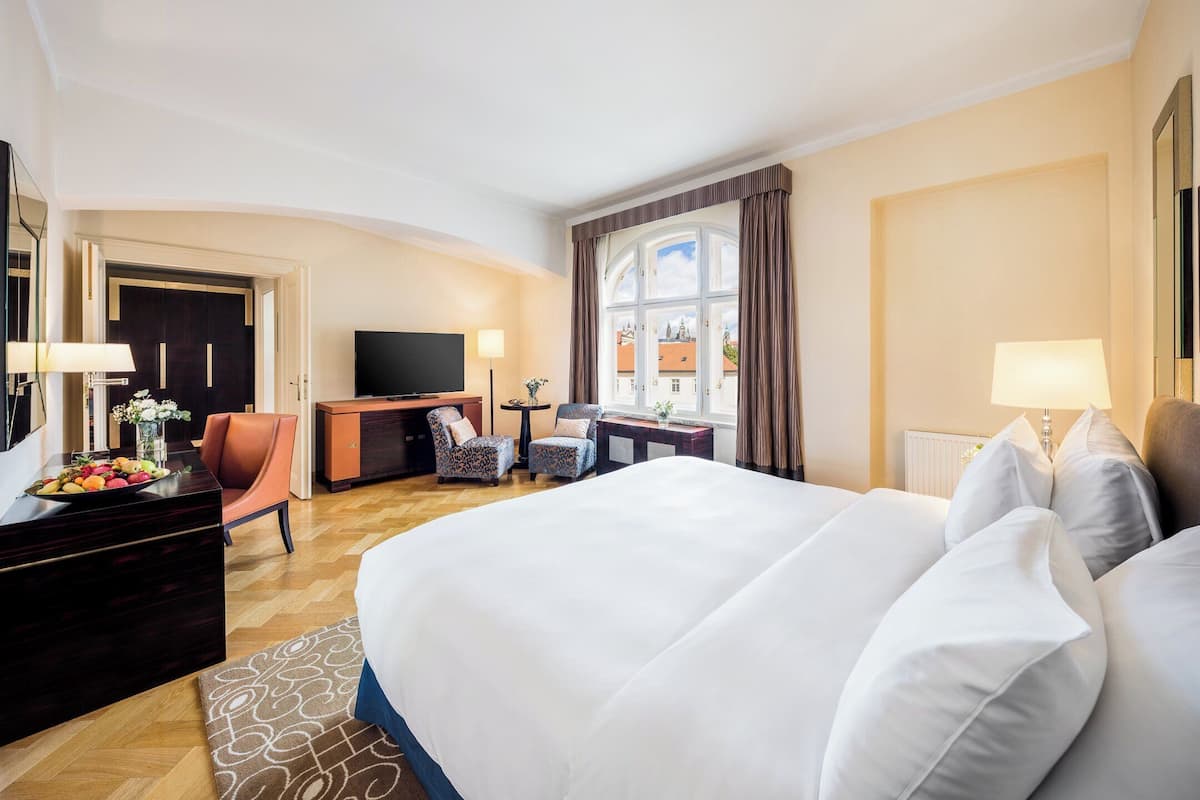A hotel room with a large bed, a desk with a TV, a chair, and a window with curtains.