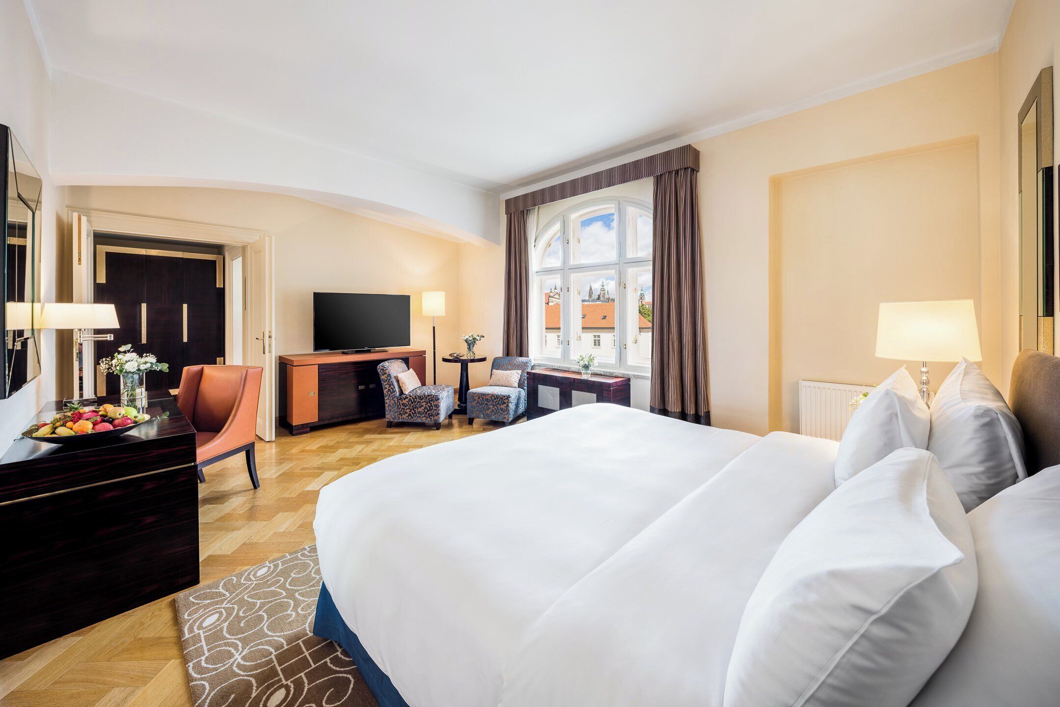 A hotel room with a large bed, a desk with a TV, a chair, and a window with curtains.