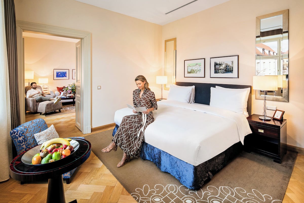 A hotel room with a large bed, a sitting area with a table, and a view of another room.