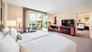 A hotel room with two beds, a desk, a television, and a view of the outside.