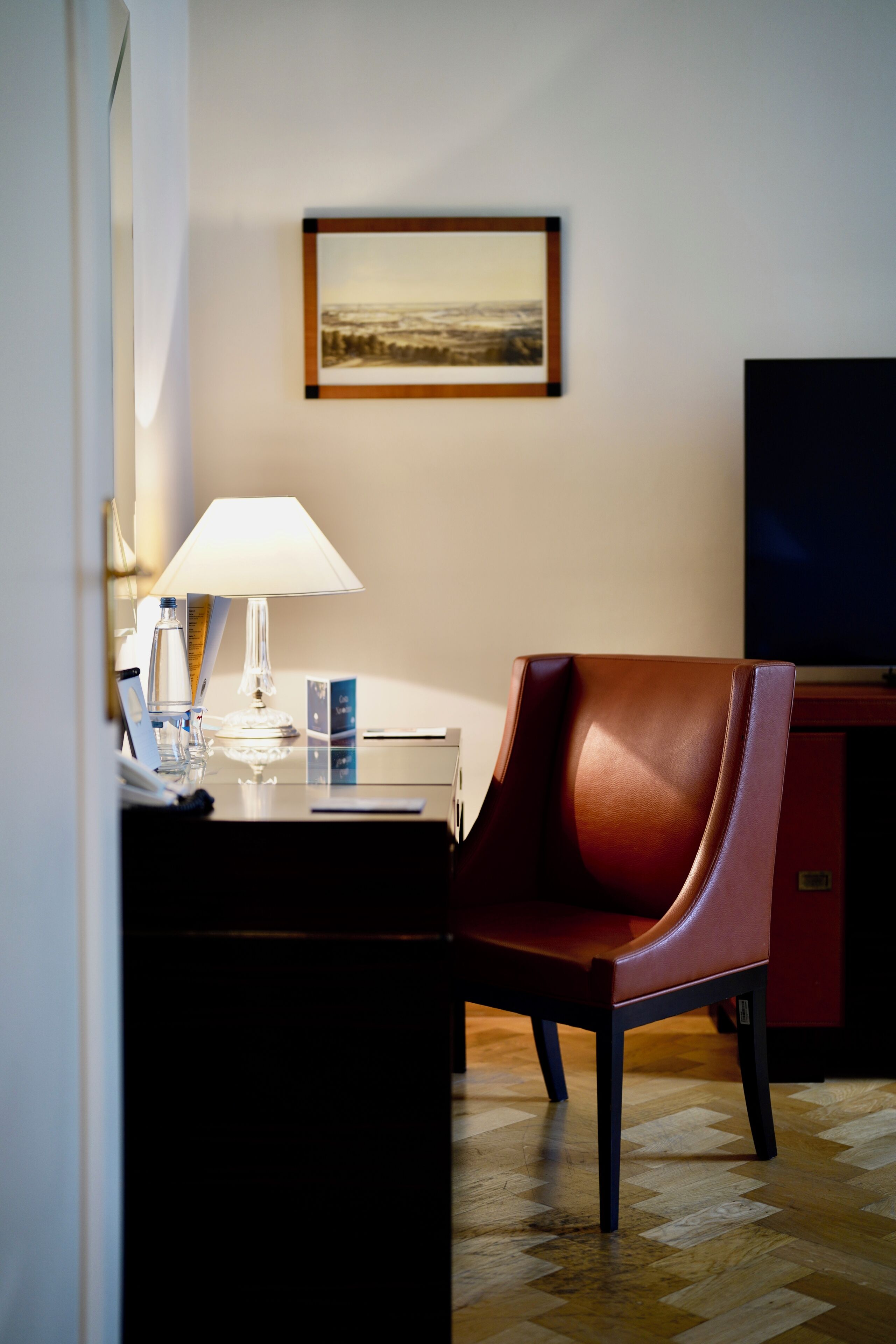 Une chambre d’hôtel équipée d’un bureau, d’une chaise, d’une lampe, d’un tableau encadré au mur et d’un téléviseur.