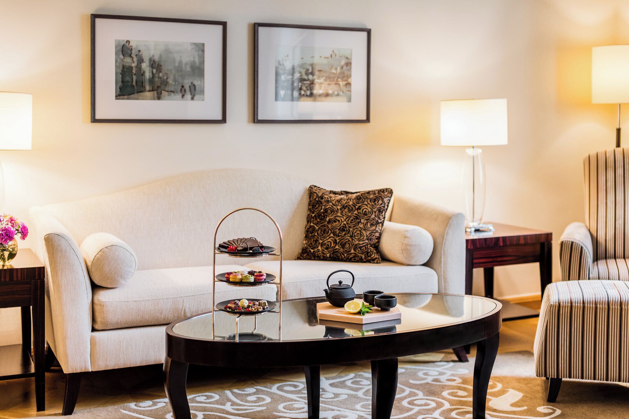 A living room with a sofa, a coffee table with a tray of snacks, a lamp, and framed pictures on the wall.