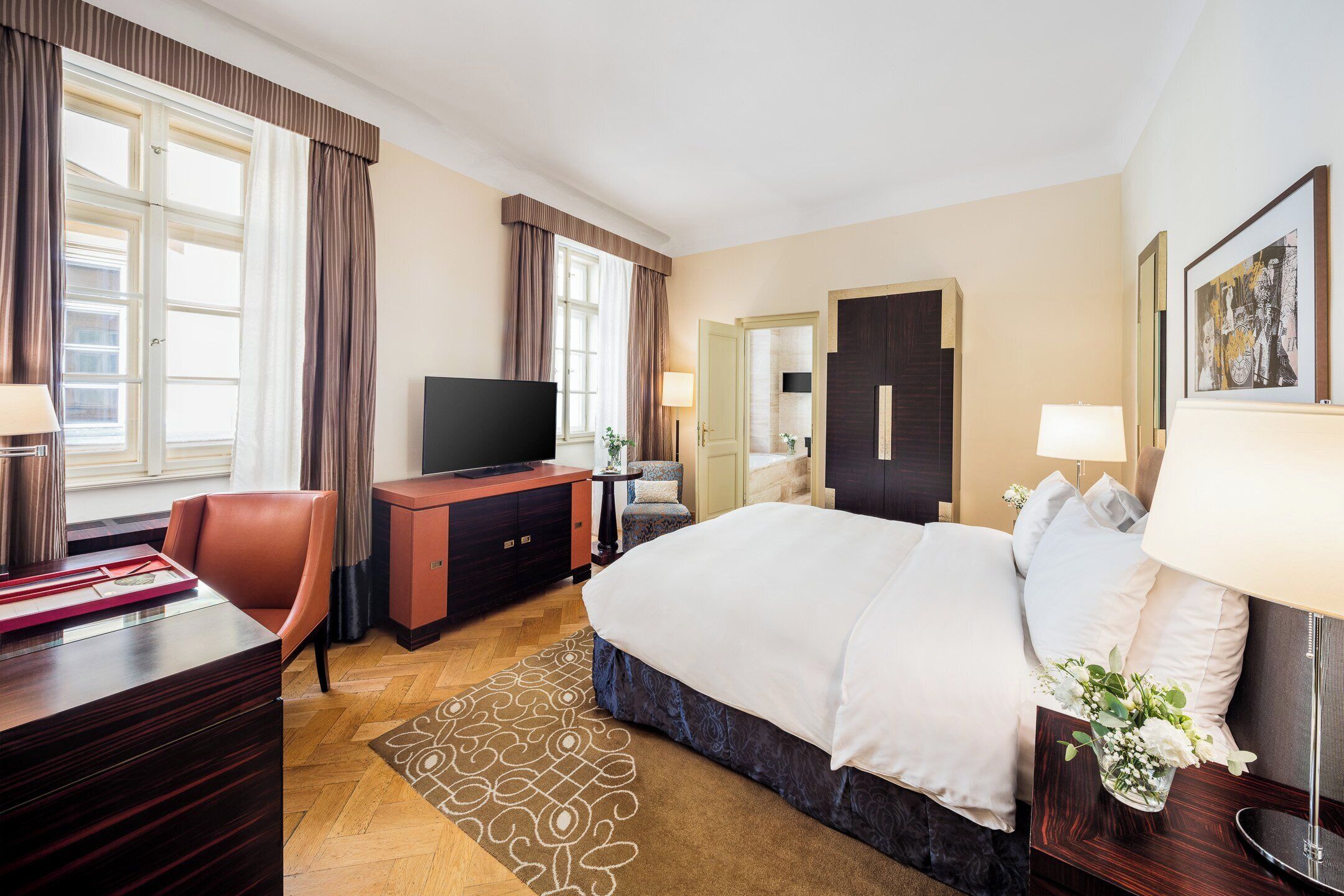 A hotel room with a bed, a desk, a television, a dresser, and a bathroom door.