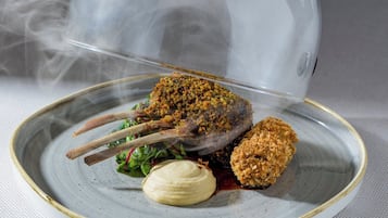 A hand holding a transparent dome over a plate with food, steam rising from the dish.