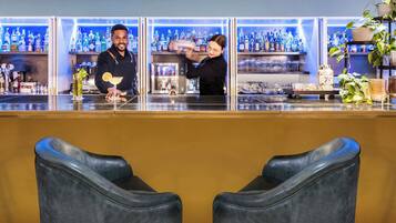Eine Bar mit zwei Barhocker, einem Barkeeper und einer gut sortierten Flaschenauswahl.