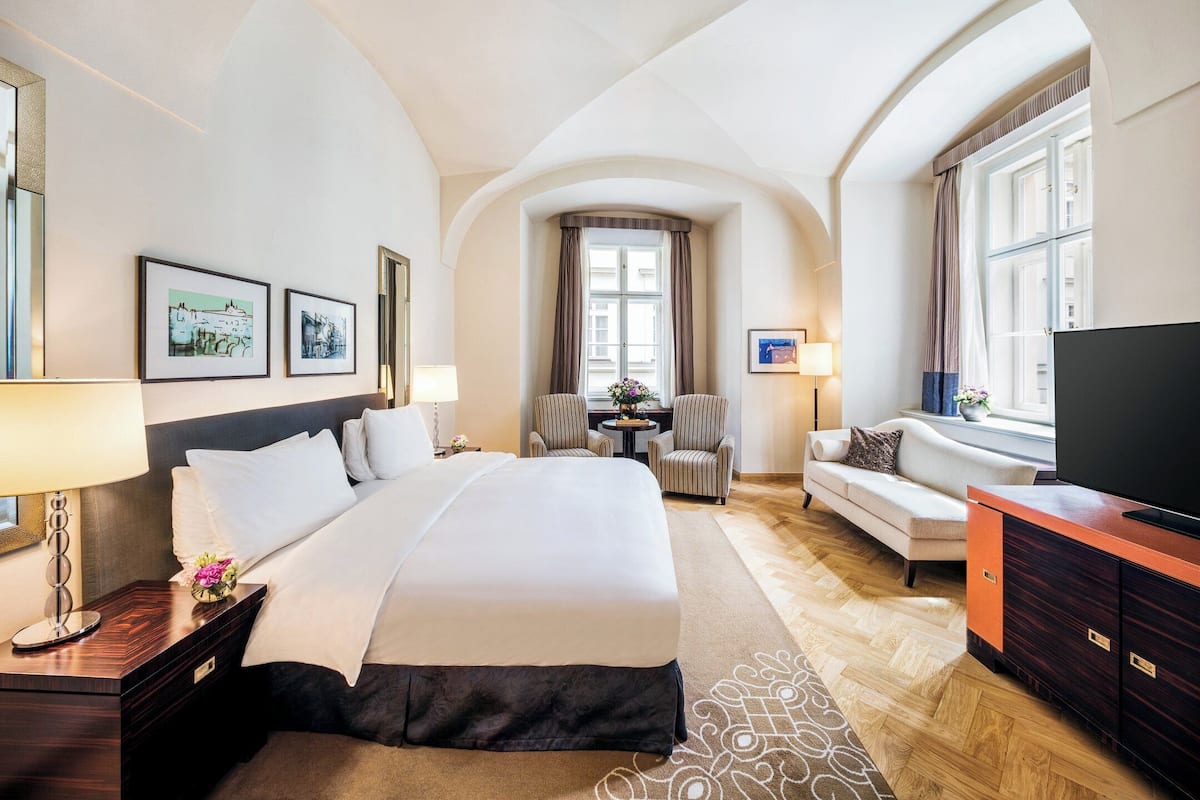 A hotel room with a large bed, a sofa, a TV, and a desk with a lamp.