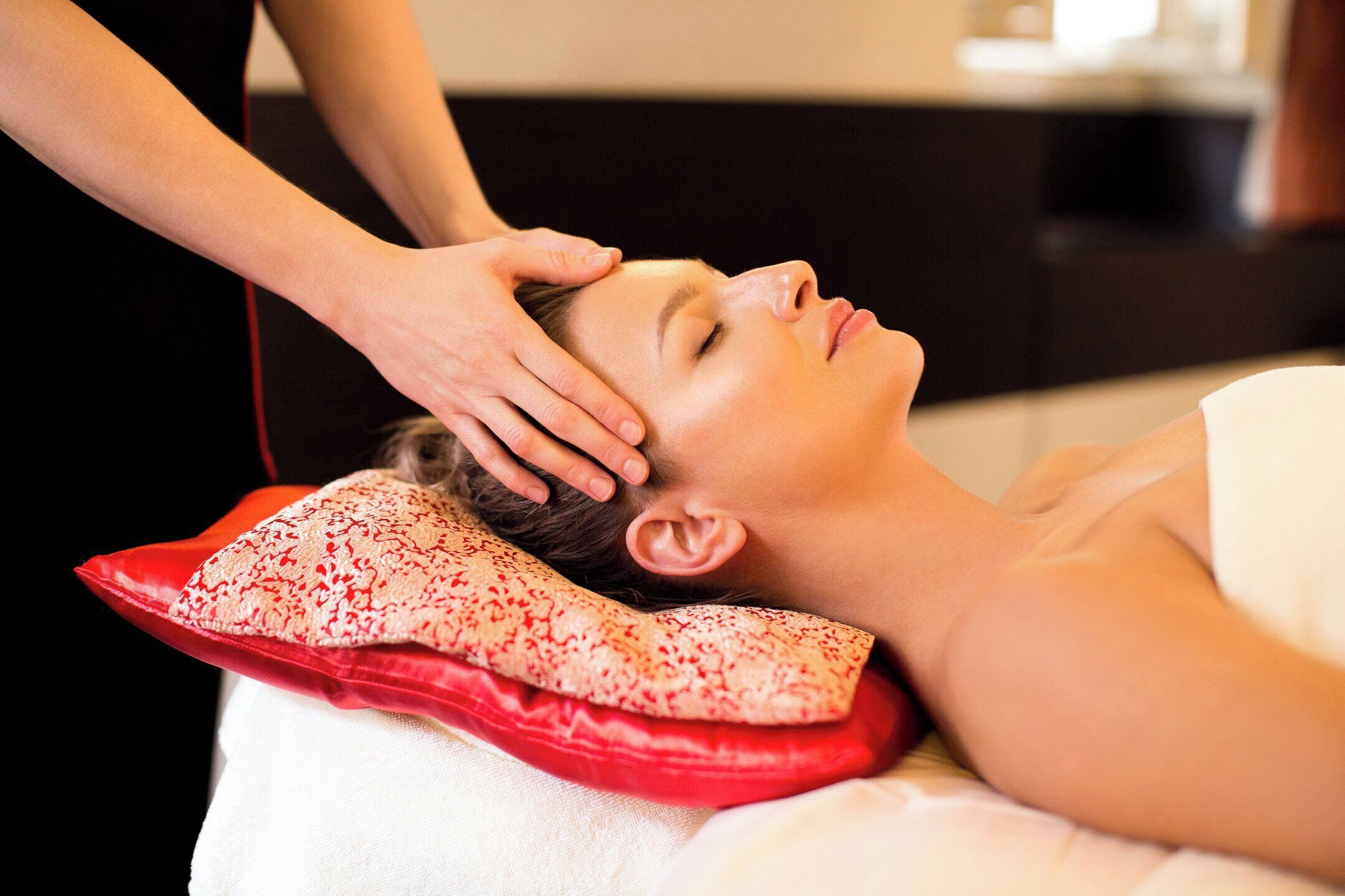A person receiving a head massage with a red pillow and a white towel.