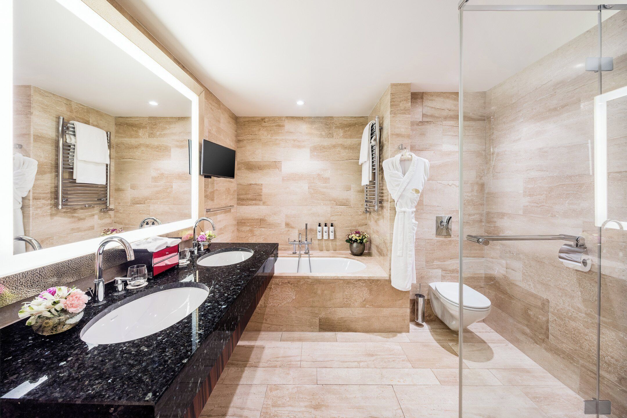 A modern bathroom with dual sinks, a large mirror, a glass-enclosed shower, and a toilet.
