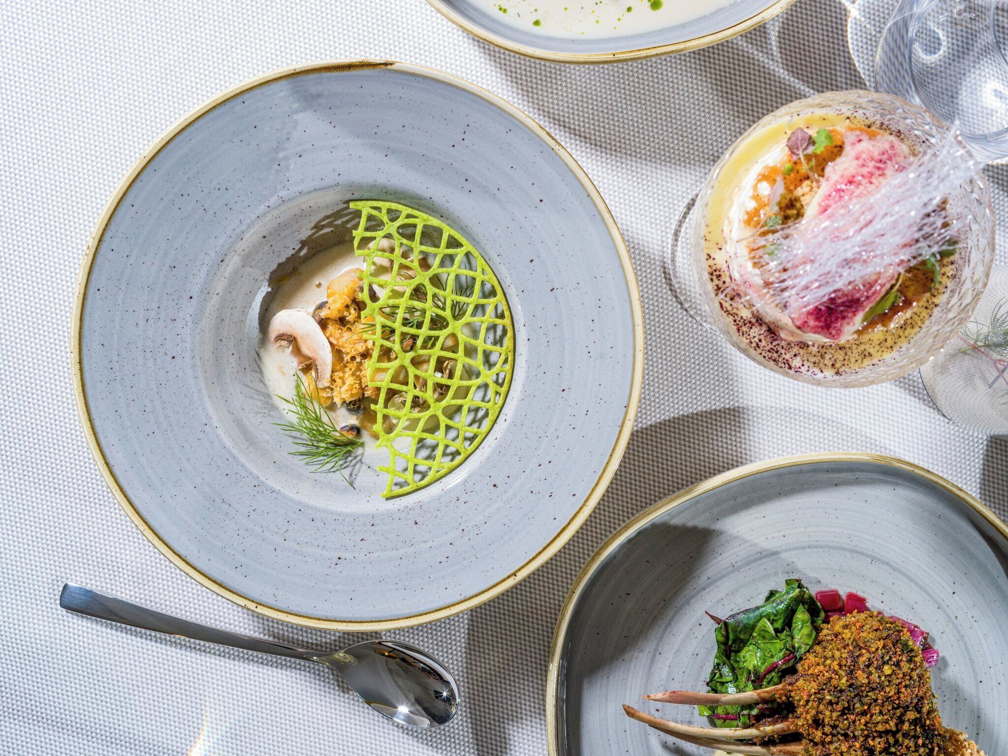 A table with three plates of food, a spoon, and a textured tablecloth.