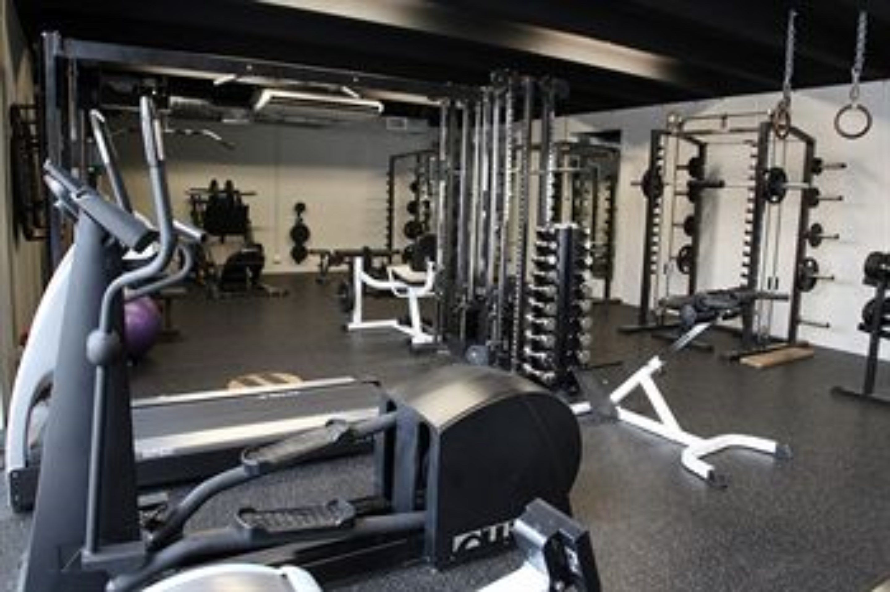Een fitnessruimte met diverse trainingsapparaten, waaronder loopbanden, krachttoestellen en losse gewichten.