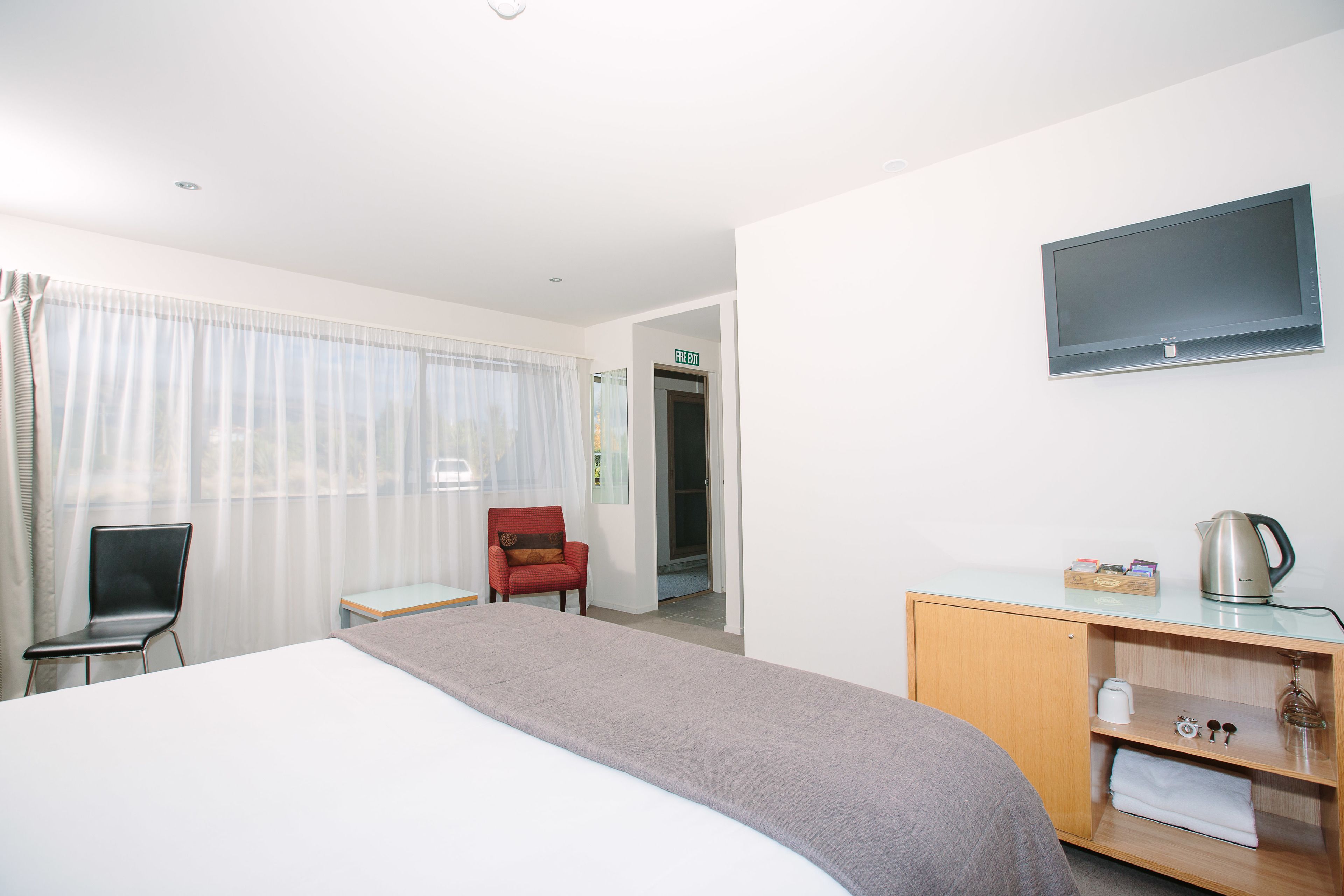 Una habitación de hotel con cama, escritorio, silla, televisor y una pequeña cocina.