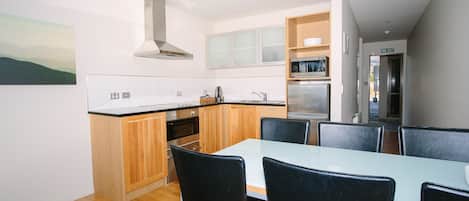 A modern kitchen with a dining area, wooden cabinets, a stainless steel range hood, and a microwave.