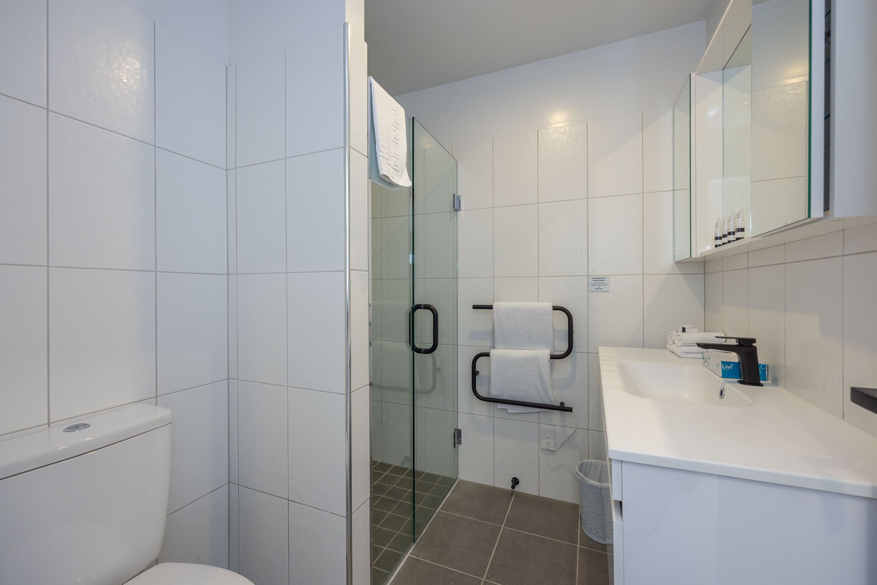 A modern bathroom with a glass-enclosed shower, white tiles, a white sink, and a mirror above the sink.