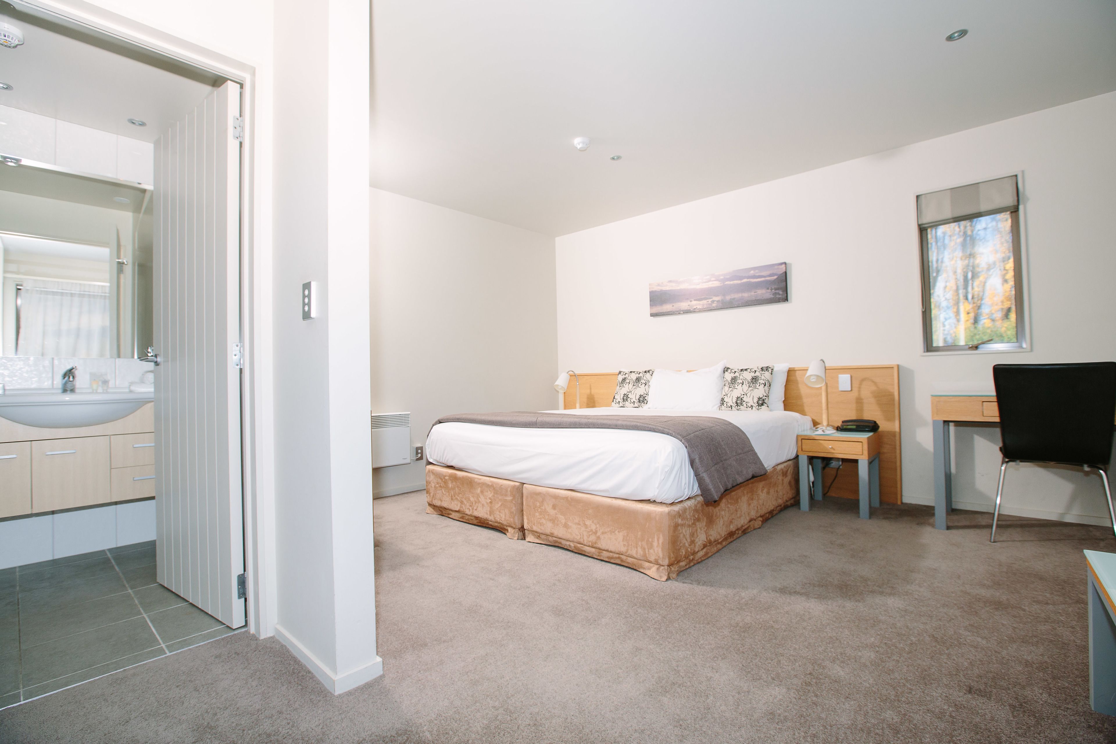 A bedroom with a bed, bedside table, chair, and a view of the bathroom.