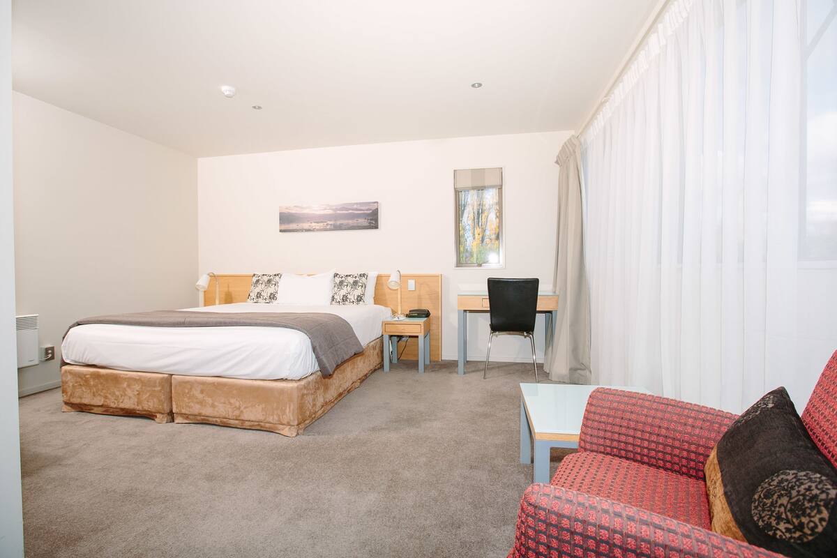 A hotel room with a bed, a desk, a chair, and a sofa.