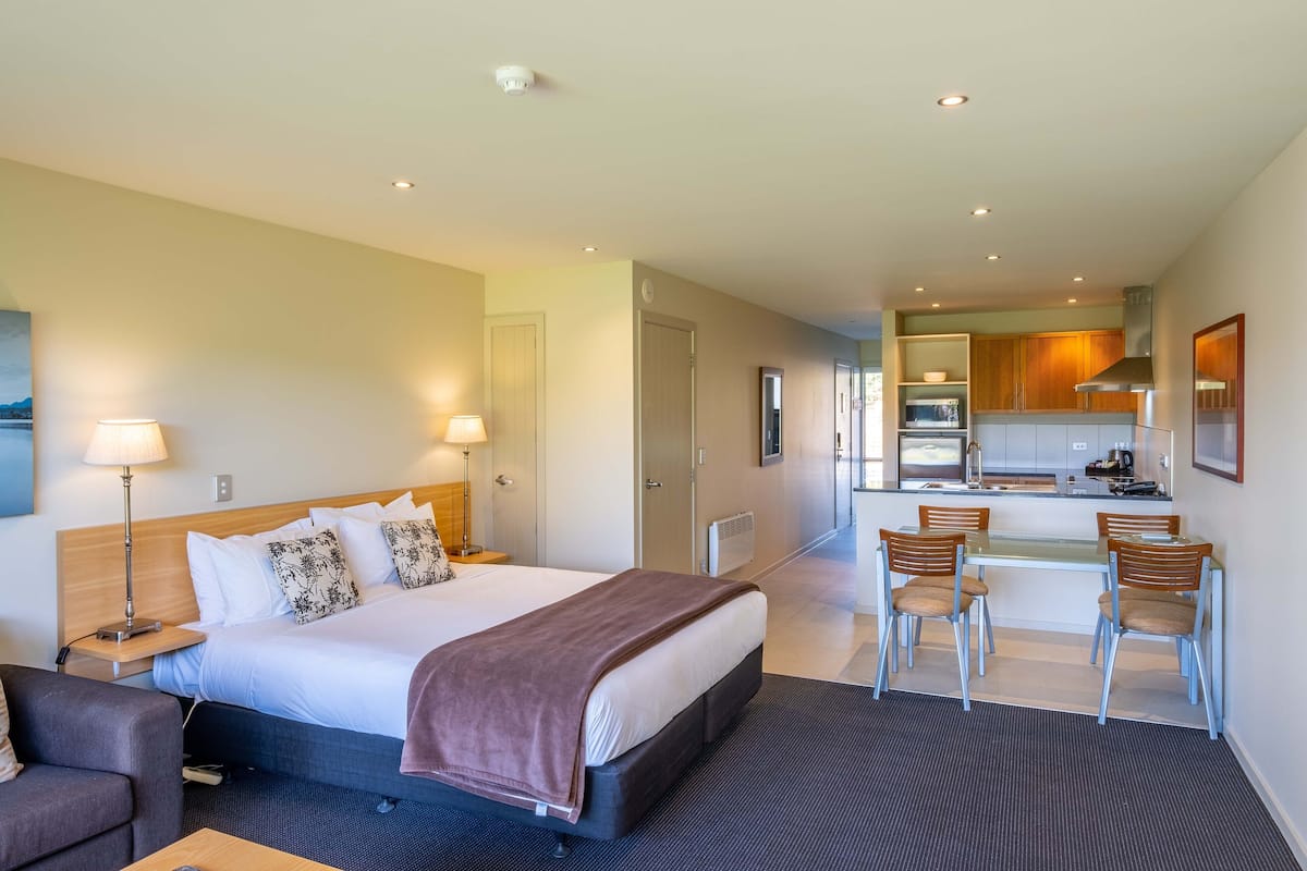 A hotel room with a bed, bedside tables, a desk, and a kitchenette.