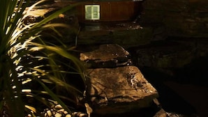 Estrutura de pedra com hidromassagem, rodeada por pedras e plantas, sob um céu noturno.