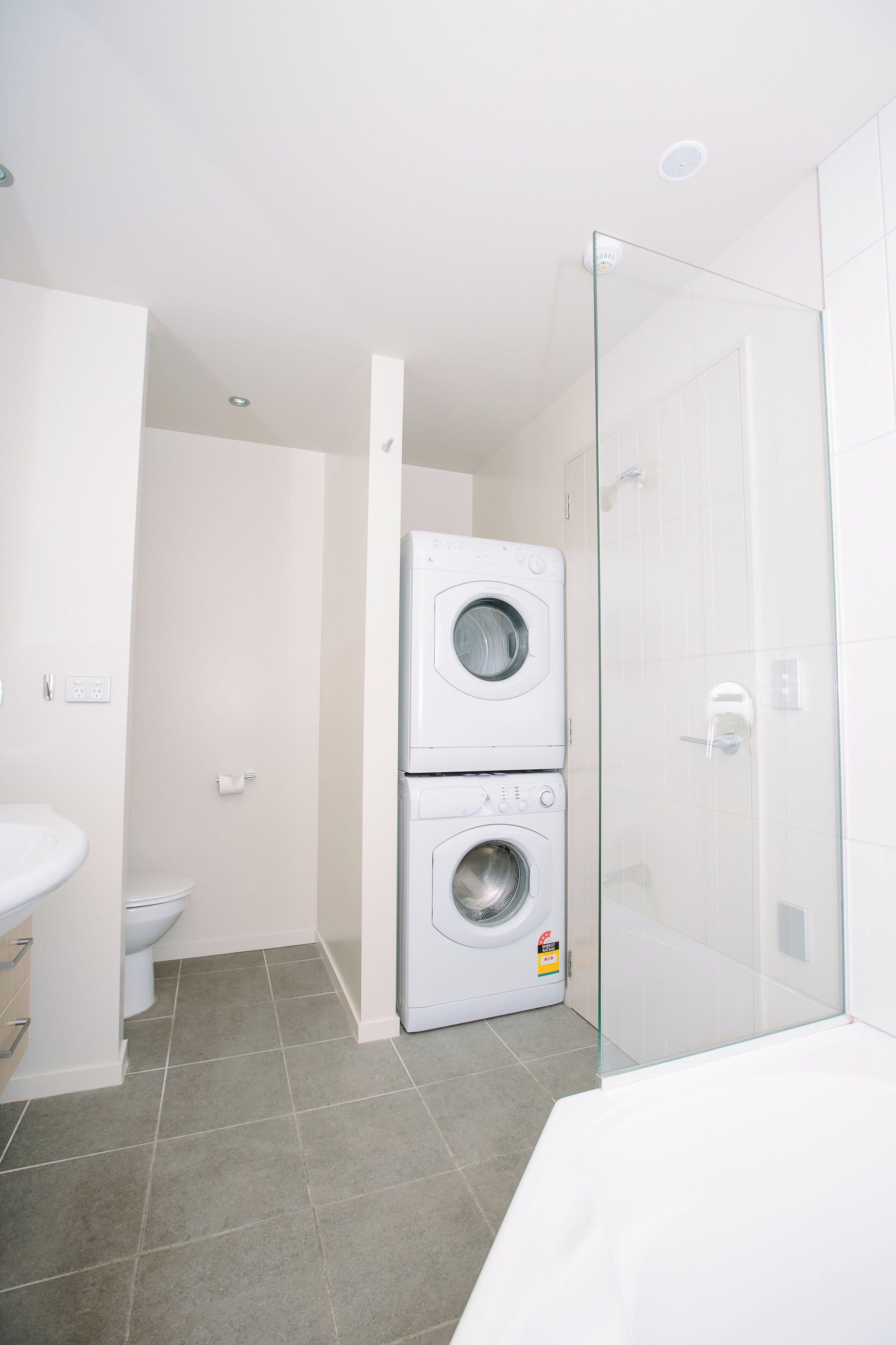 Une petite salle de bain équipée d’un lave-linge, de toilettes et d’une douche à parois en verre.