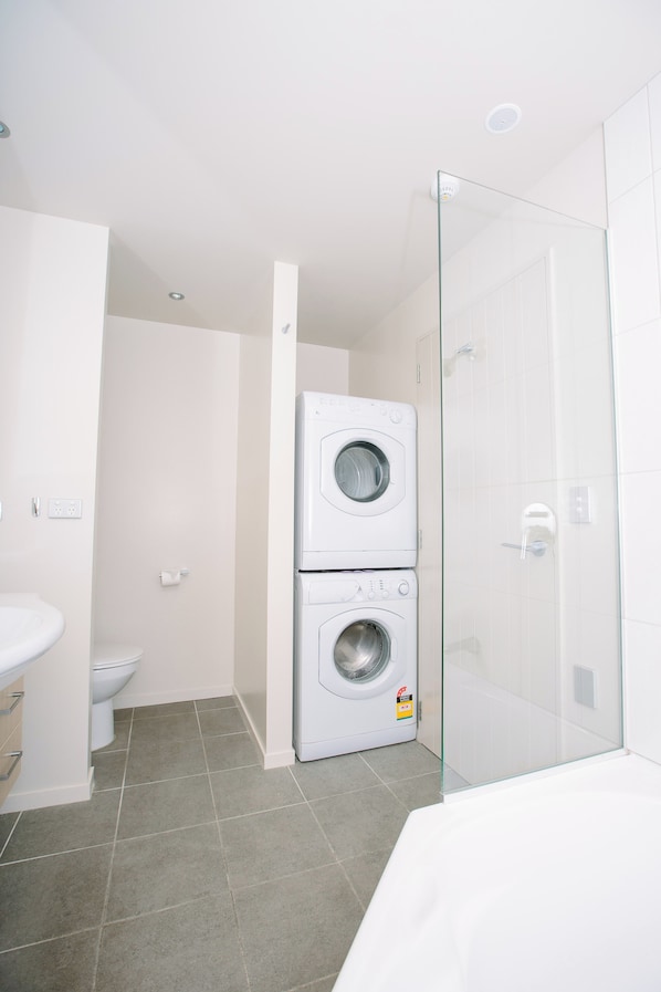 A compact bathroom with a washing machine, a toilet, and a glass shower enclosure. - Oakridge Resort Lake Wanaka (Wanaka)