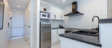 A modern kitchen with white cabinets, a stainless steel refrigerator, a microwave, and a built-in oven.