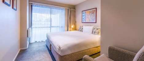 A hotel room with a large bed, a chair, a painting on the wall, and a window with curtains.