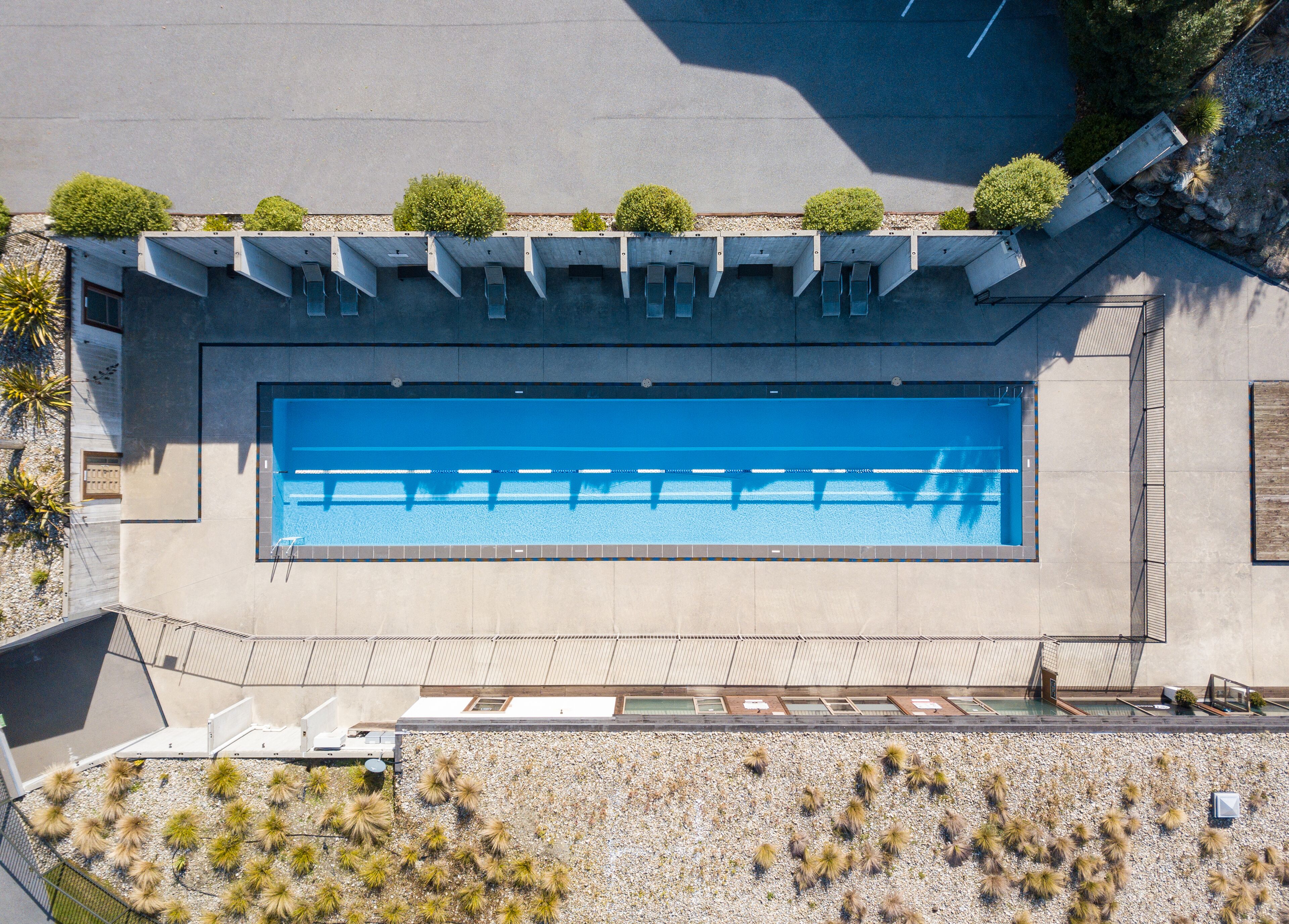 Una gran piscina rectangular con superficie de agua azul cristalina, rodeada por un patio de concreto y un muro de piedra bajo.