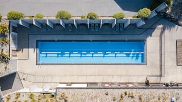A large rectangular swimming pool with a clear blue water surface, surrounded by a concrete deck and a low stone wall.