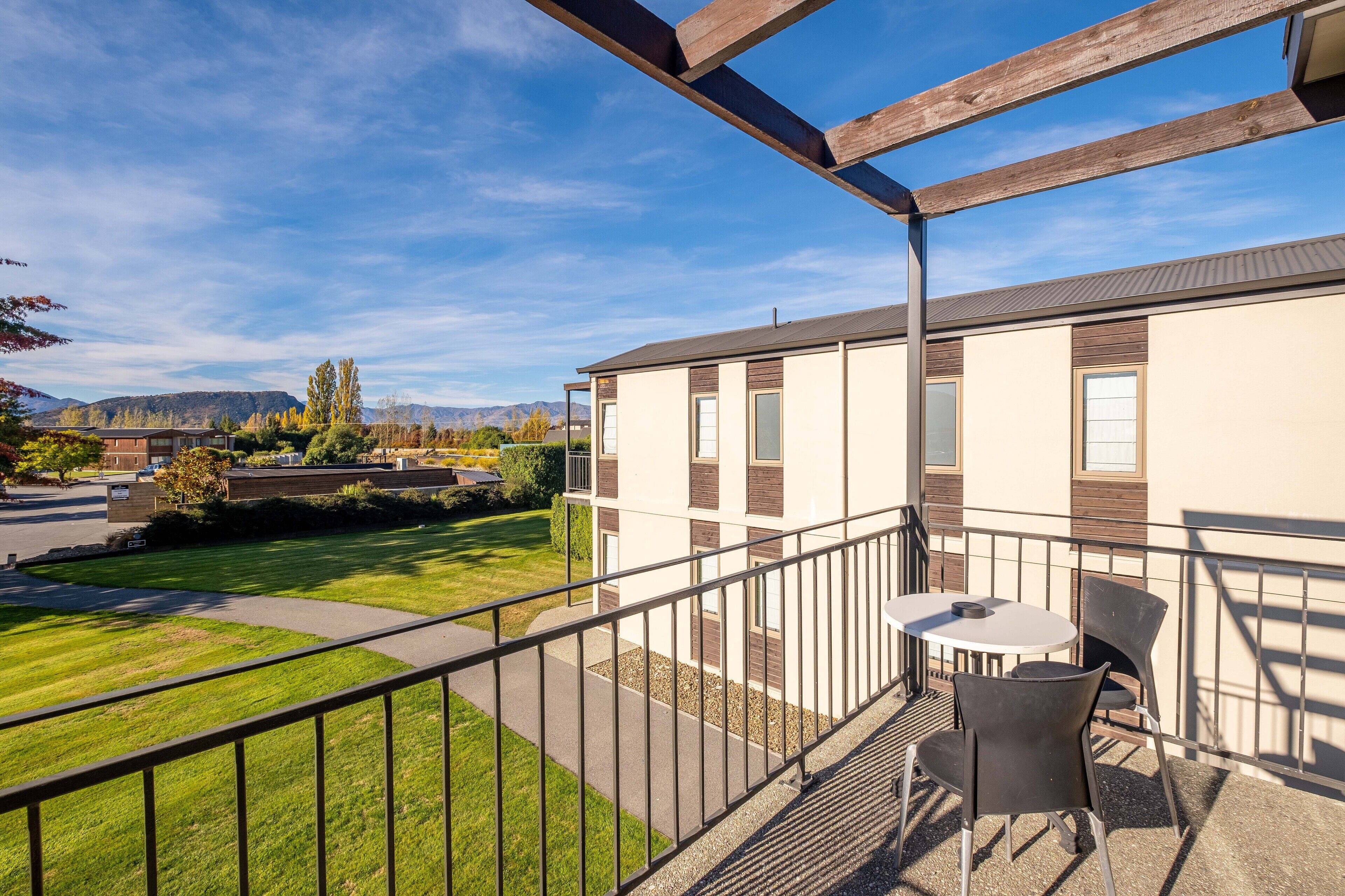 A balcony with a table and chairs, overlooking a well-maintained lawn and a building with a modern design.