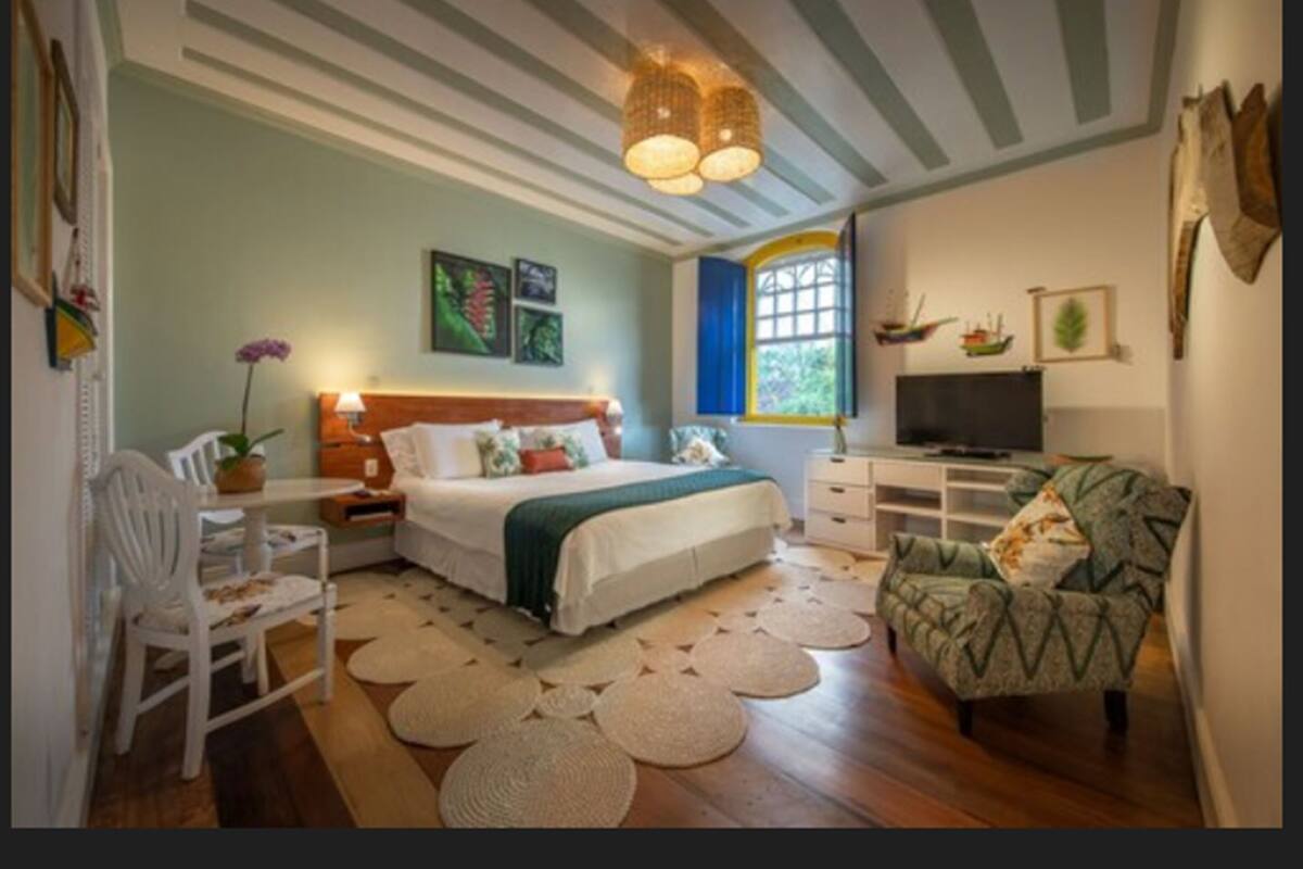 A bedroom with a bed, bedside tables, a chair, a television, and a window.