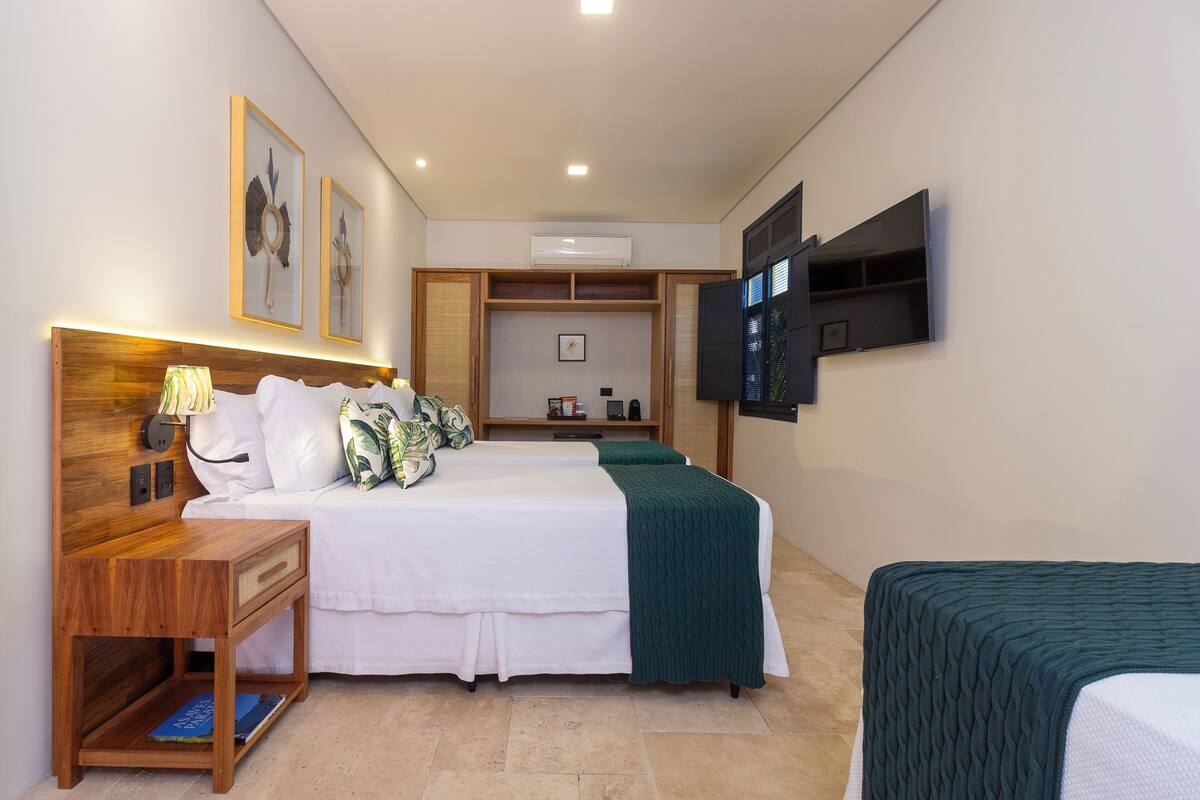 A hotel room with a bed, bedside table, lamp, and a TV mounted on the wall.