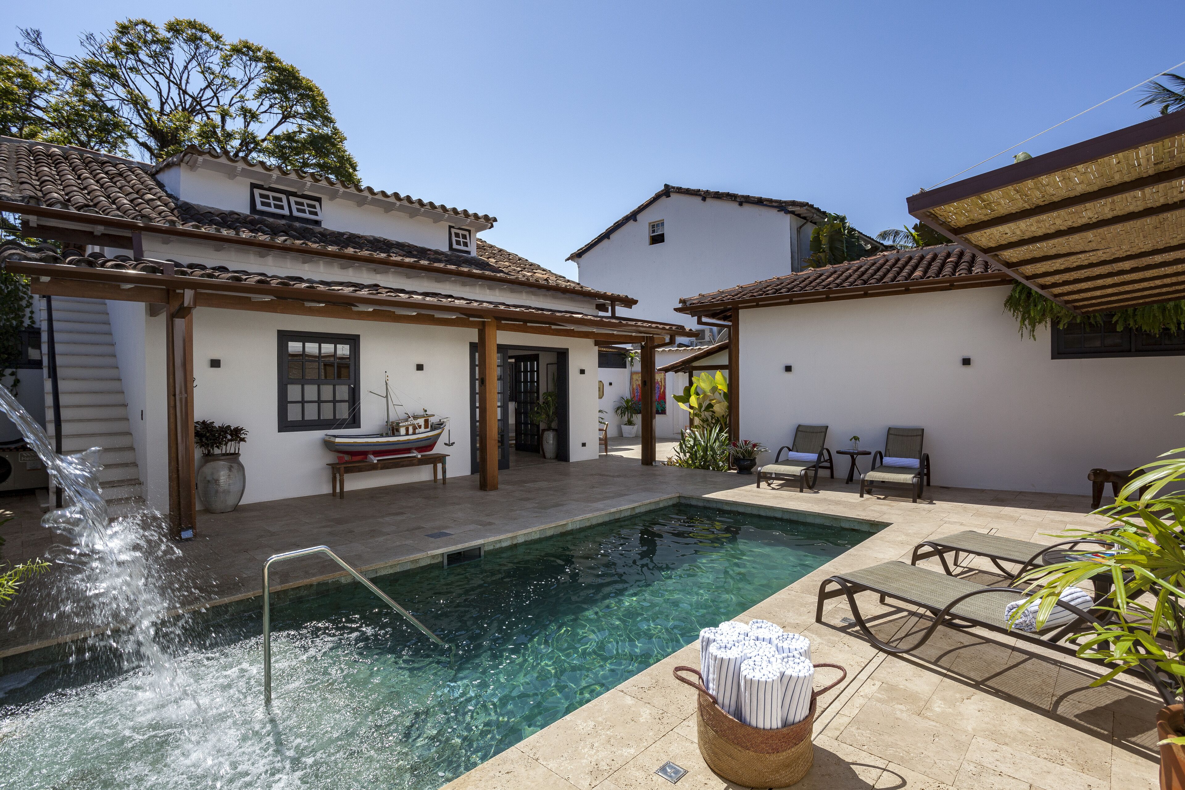 A swimming pool area with a pergola, lounge chairs, and a small boat model.