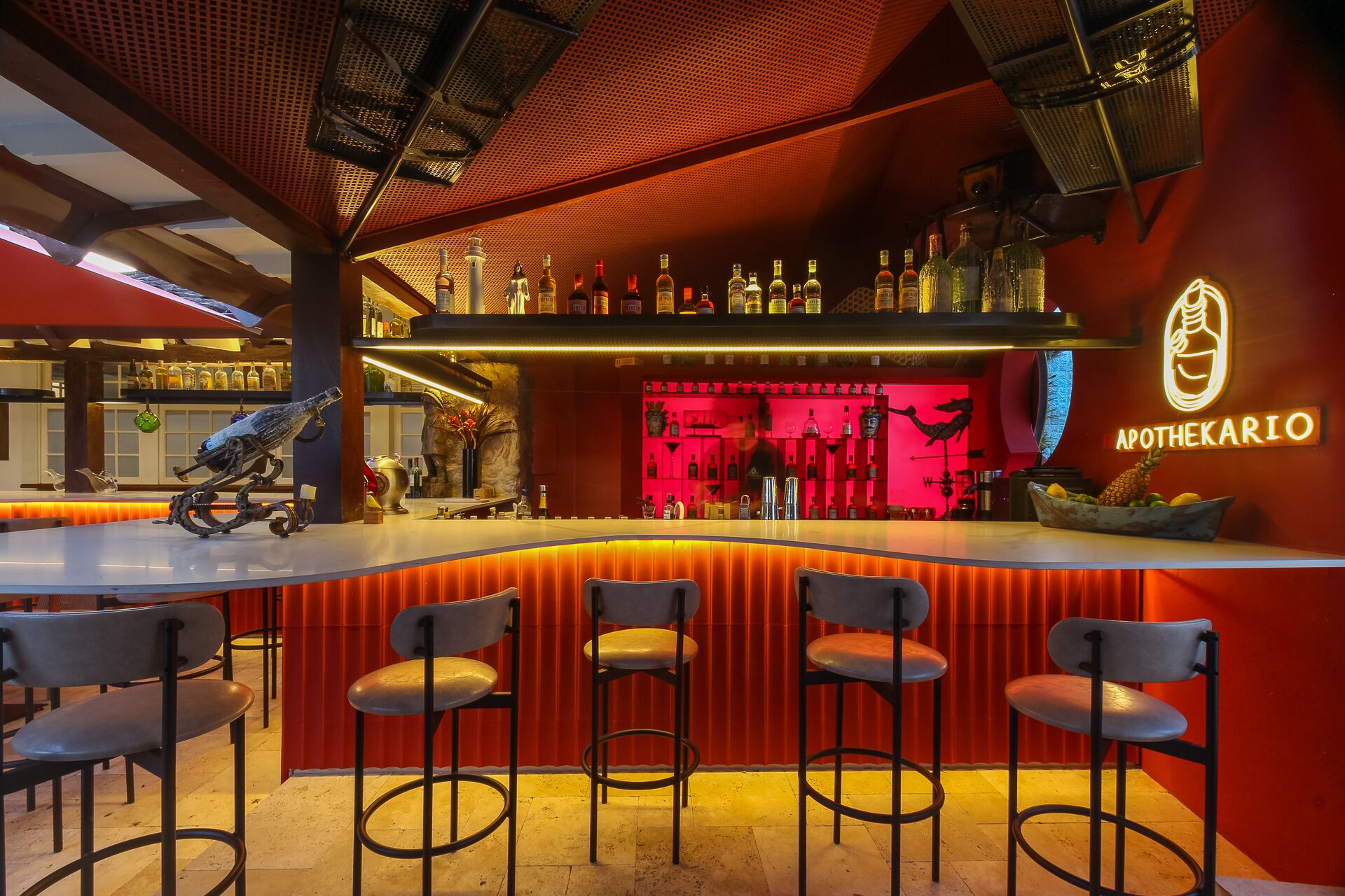 Een barruimte met een kleurenschema in rood en oranje, barstoelen en een verscheidenheid aan flessen en glazen op planken.