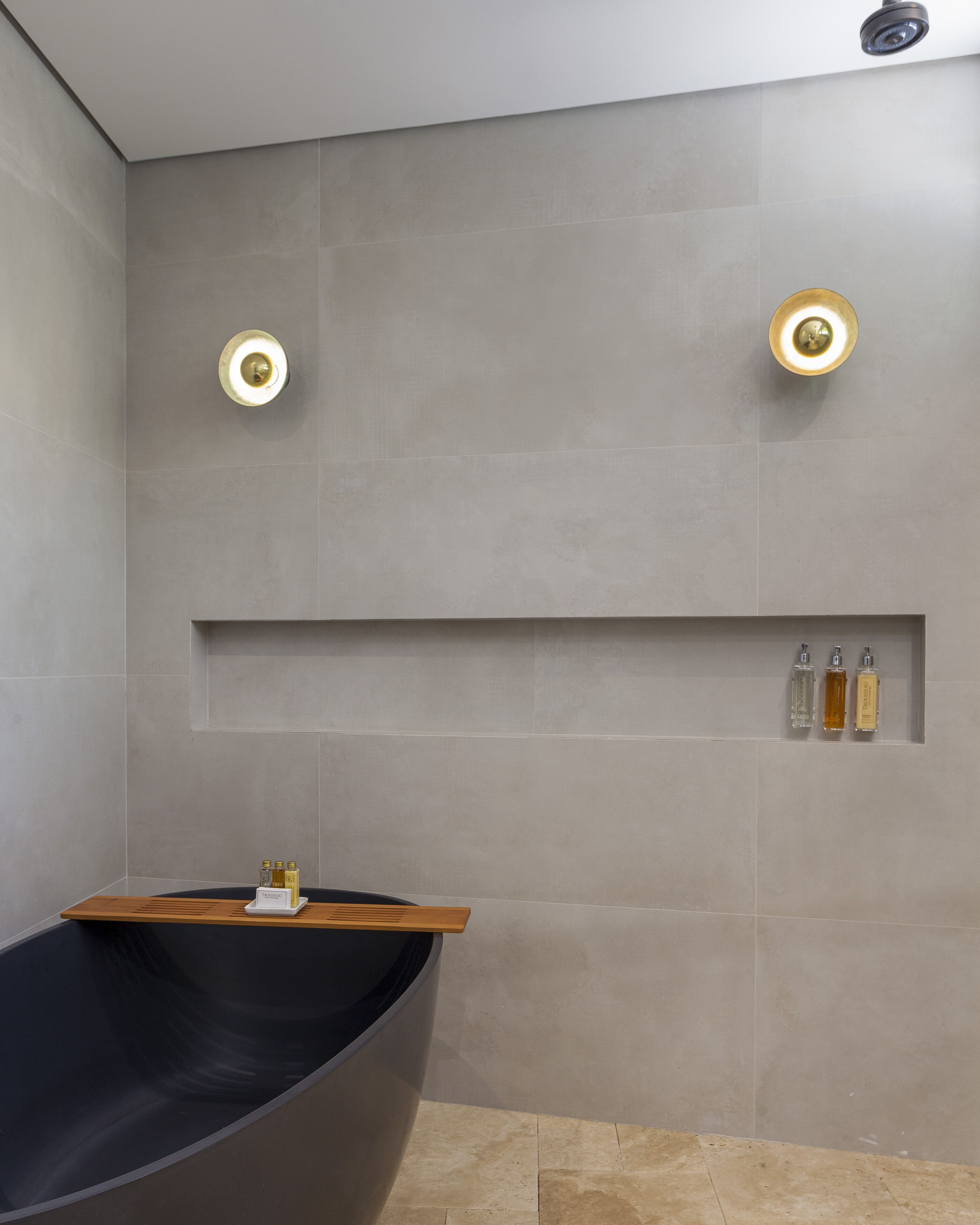 Un baño moderno con una bañera independiente, iluminación empotrada y un estante con artículos de aseo.