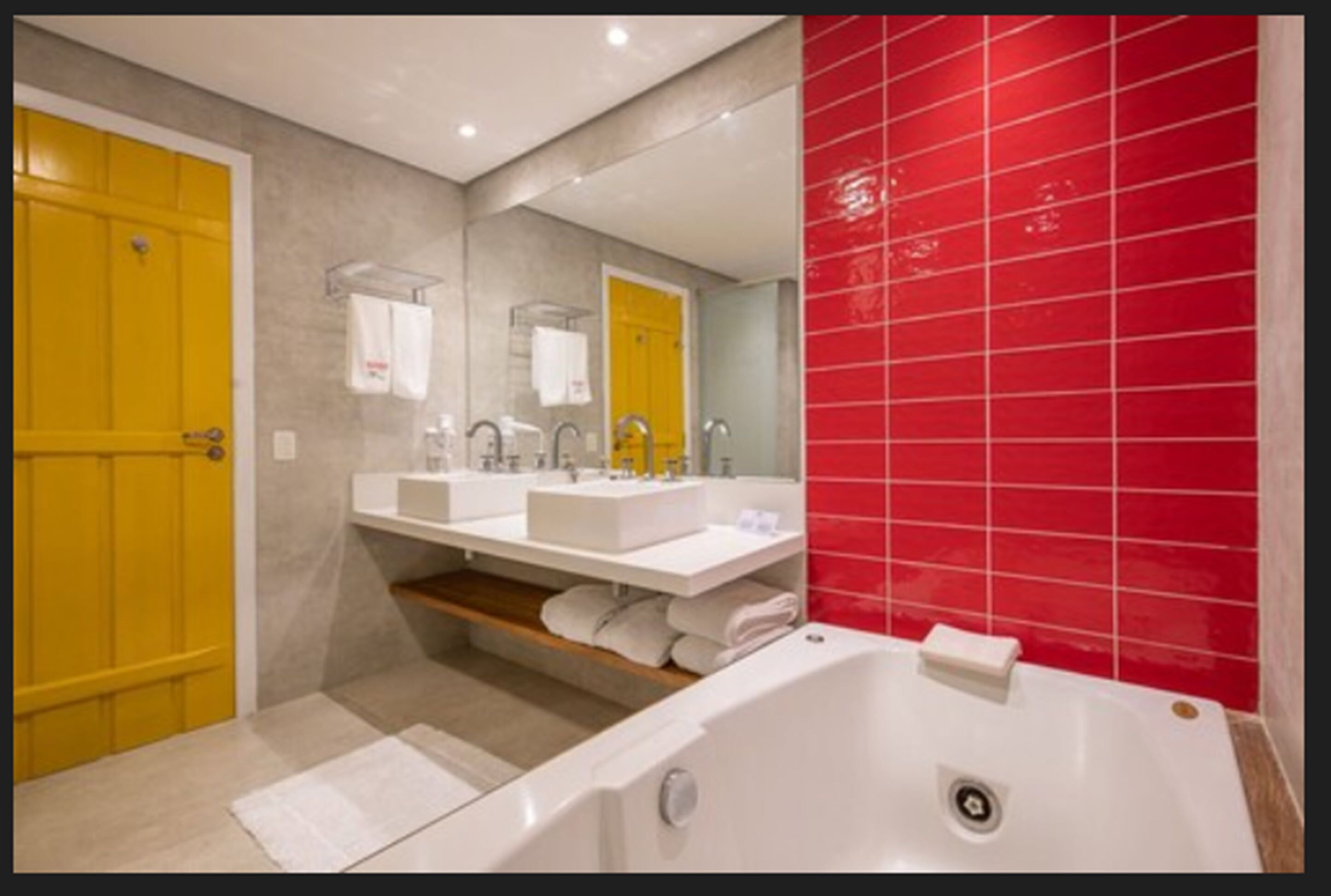 A modern bathroom with two sinks, a bathtub, and a red-tiled wall.