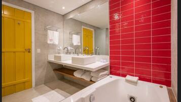 A modern bathroom with two sinks, a bathtub, and a red-tiled wall.