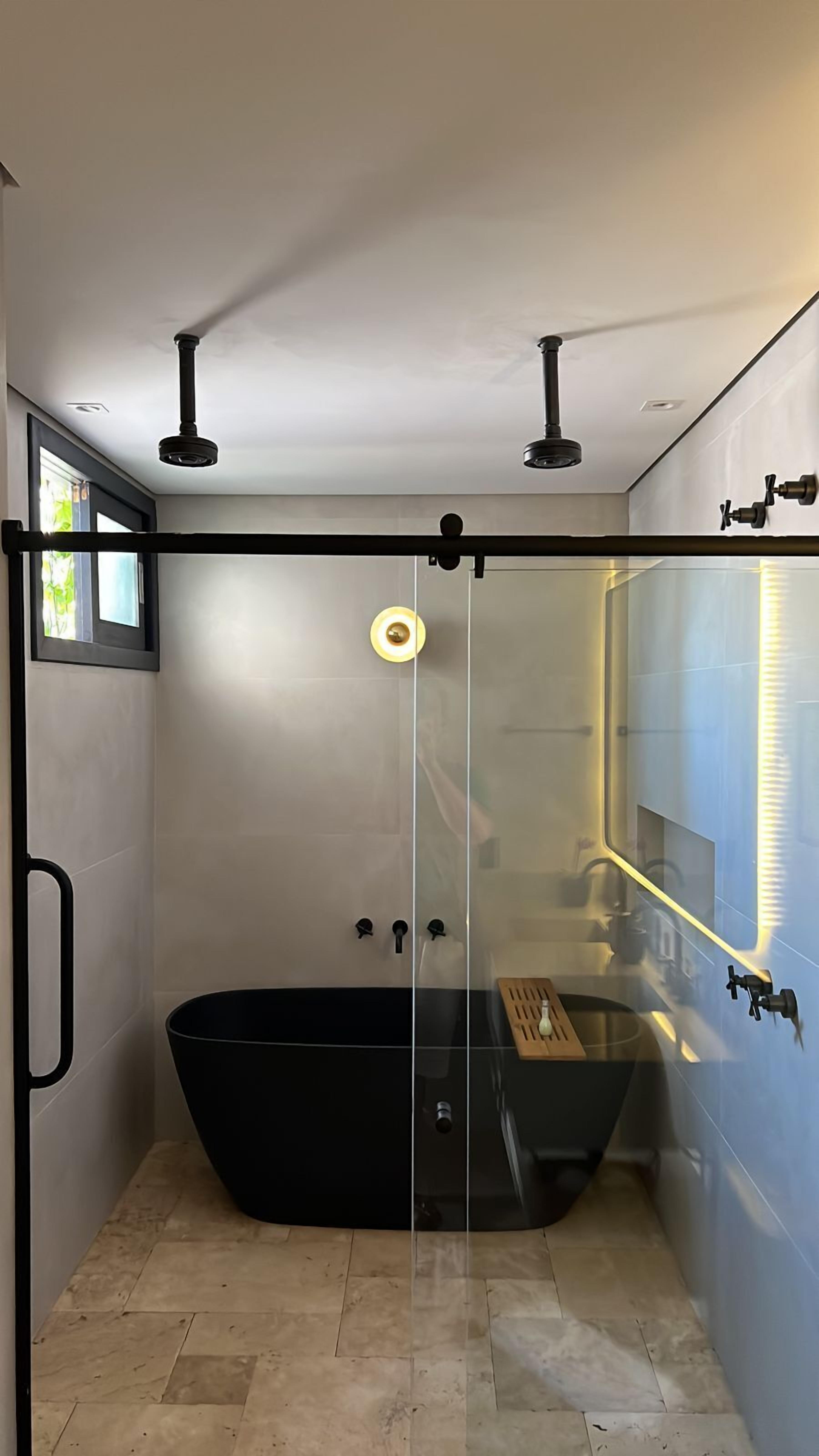 Casa de banho moderna com banheira de hidromassagem separada por vidro, zona de duche e janela que permite entrada de luz natural.