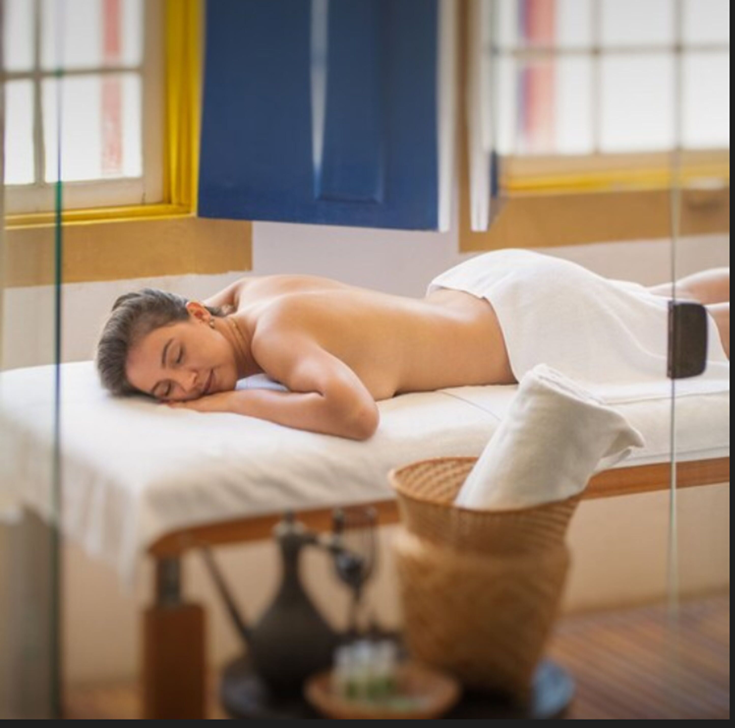 A person lying on a massage table in a room with a window and a wooden floor.