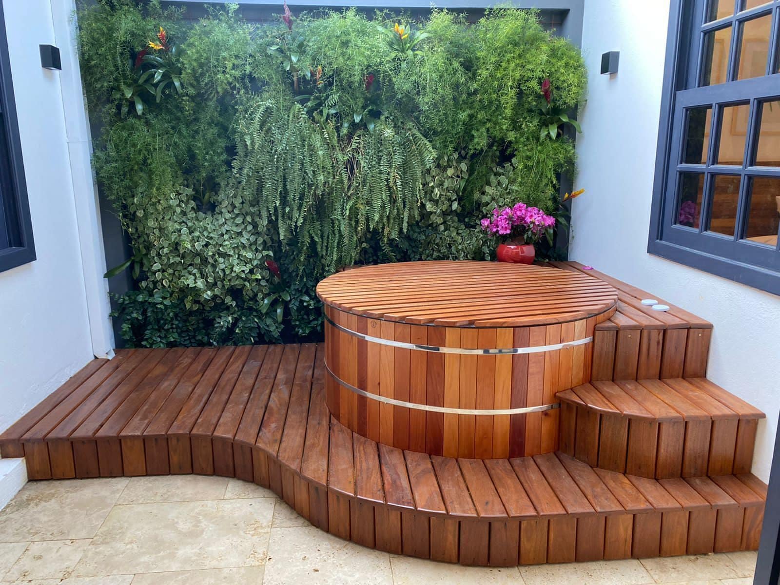 Un bain à remous en bois, doté de marches, entouré d’un mur végétal luxuriant composé de différentes plantes.