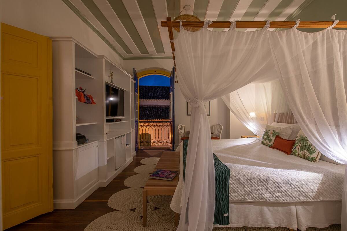 A bedroom with a canopy bed, a TV, a bookshelf, and a view of a balcony.