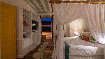 Un dormitorio con cama a dosel, televisor, estantería y vistas a un balcón.