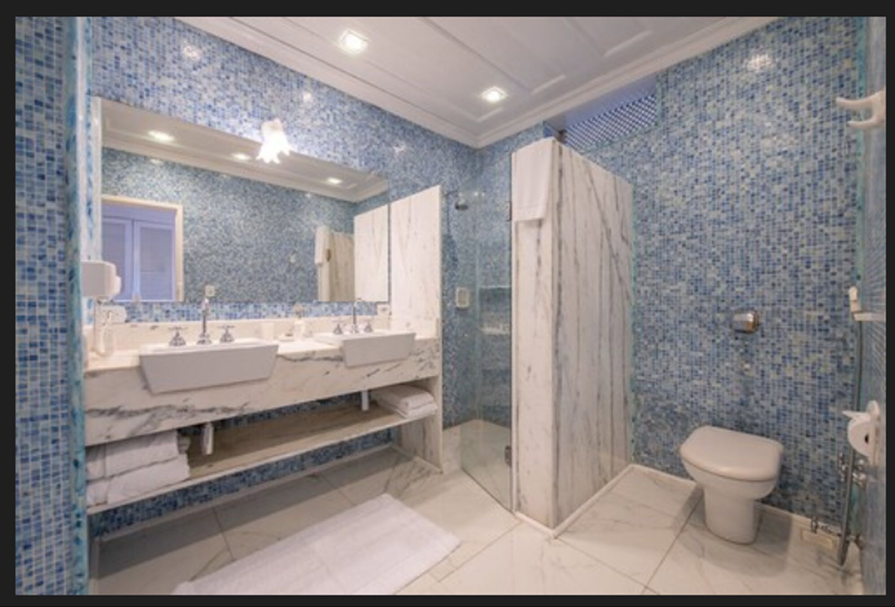 A bathroom with a marble vanity, two sinks, a large mirror, a shower enclosure, and a toilet.