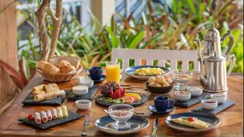A breakfast table set with various dishes, including eggs, toast, and fruit, with a coffee pot and a view of greenery outside.
