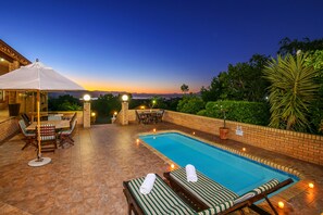 A swimming pool with lounge chairs and a table, surrounded by a brick wall and greenery. - Amber Guest Lodge (Knysna)